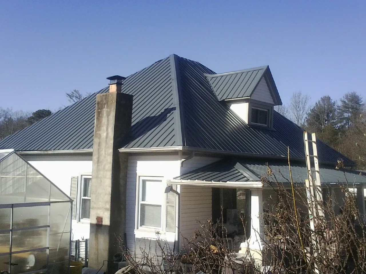 Dark blue standing seam metal roof on a white farmhouse with dormer — Slate & Tile Roof Repair by Roofing Brothers in Garrison