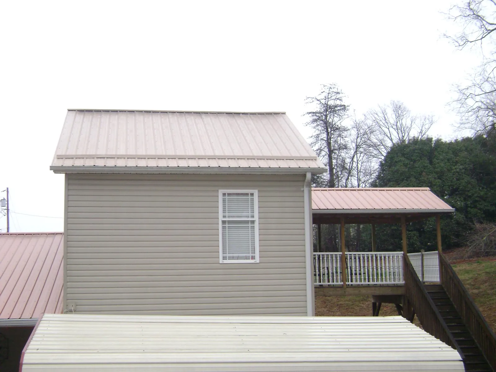 Tan metal roofs on a two story addition and attached porch, from a Roof Replacement job in Garrison